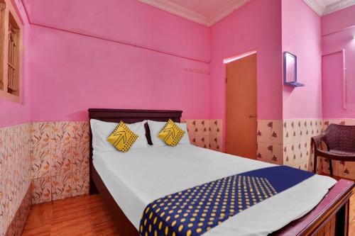 a bedroom with pink walls and a bed with yellow pillows at SPOT ON Sri Maheswari Lodge in Vijayawāda