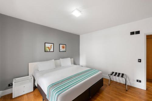 a white bedroom with a bed and a chair at Capcana Hotel Jardins in Sao Paulo
