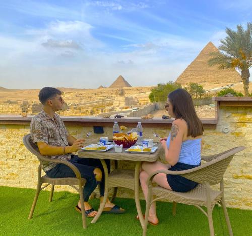 um homem e uma mulher sentados numa mesa em frente às pirâmides em Seven Pyramids Inn em Cairo