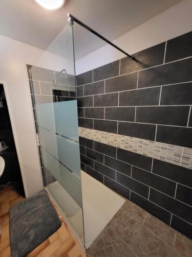 y baño con ducha de cristal y azulejos negros. en La maison du Perrin, en Gréez-sur-Roc