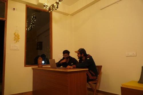 dos hombres sentados en un escritorio con un portátil en Firefly Hostel en Manāli