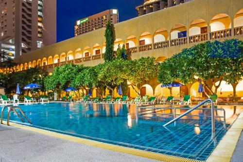 a swimming pool with chairs and trees in front of a building at S Lodge Pattaya formally Sabai Lodge in Pattaya