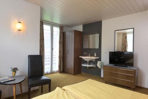 a room with a bed and a television and a table at Hotel Bel-Air Eden in Grindelwald