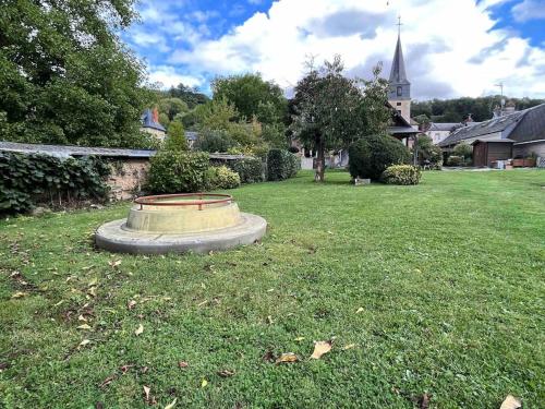 un parc avec un monument dans l'herbe et une église dans l'établissement « Au Fil du Bec », au Bec-Hellouin