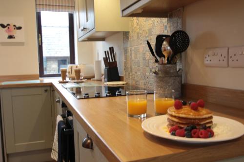 a plate of pancakes and fruit on a counter with glasses of orange juice at Moo Cow Cottage Self Catering in Oakham