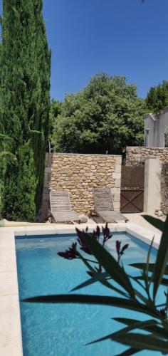une piscine avec deux chaises et un mur en pierre dans l'établissement La Closerie de la Cèze, à Cornillon
