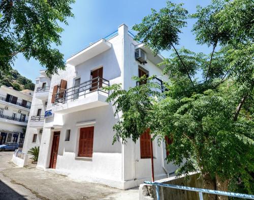 a white building with red doors and trees at To Gefyraki Rooms in Agios Kirykos