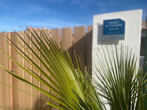 a green plant in front of a fence with a sign at HOOliRé17 3étoiles in Ars-en-Ré