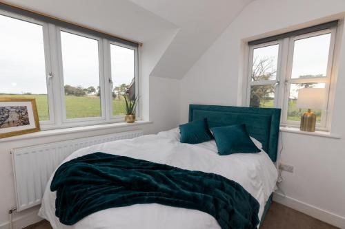 a bedroom with a bed with a green headboard and windows at The Poppies Cottage in Six Mile Bottom