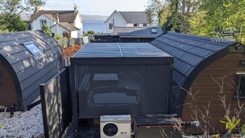 a black shed with a roof and a house at Beach House Pods in Dunoon