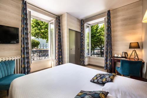 a bedroom with a bed and a desk and two windows at Hotel Beau Rivage in Aix-les-Bains