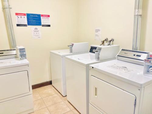 eine Waschküche mit vier weißen Waschmaschinen und Waschbecken in der Unterkunft Days Inn by Wyndham Grande Prairie in Grande Prairie