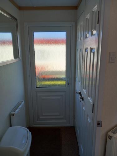 a bathroom with a toilet and a window and a door at Melody Brooks Caravan Park Caravan number 22 in Portknockie