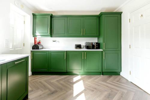 a green kitchen with green cabinets and a wooden floor at Luxury 5 Bed house in the City, includes parking & EV point in Norwich