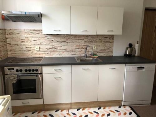 a kitchen with white cabinets and a sink and a stove at Apartmán s terasou a zahradou na cyklostezce in Havlovice