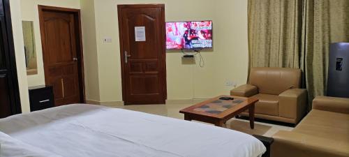 a hotel room with a bed and a chair and a tv at Joyous AP Guest House in Aburi