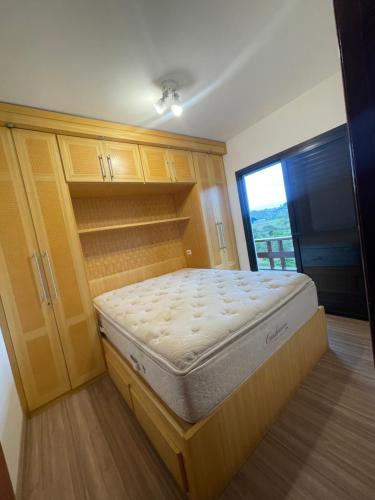 a bedroom with a bed and wooden cabinets and a window at Piemonte Flat Serra Neg SP in Serra Negra