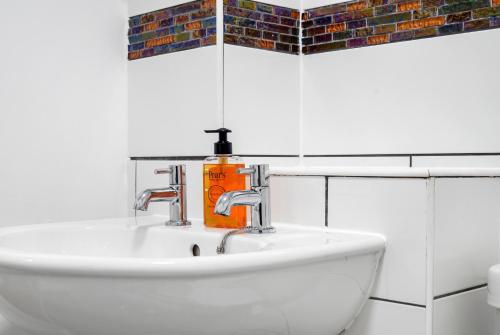 a bathroom sink with an orange soap bottle on it at Beautiful 2 Bedroom Apartment MK Free Parking in Woolstone