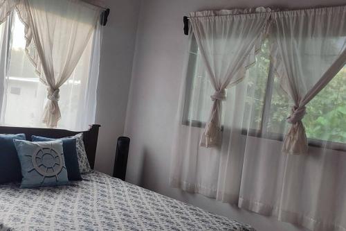 a bedroom with a bed and two windows with curtains at Villa Marina, Nosara in Río Seco