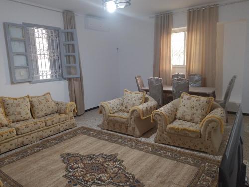 a living room with couches and a table and windows at Meilleure Escale à Gabes in Al Mayyitah