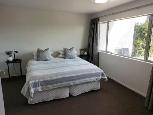 a white bedroom with a bed and a large window at Bethlehem Apartment in Tauranga