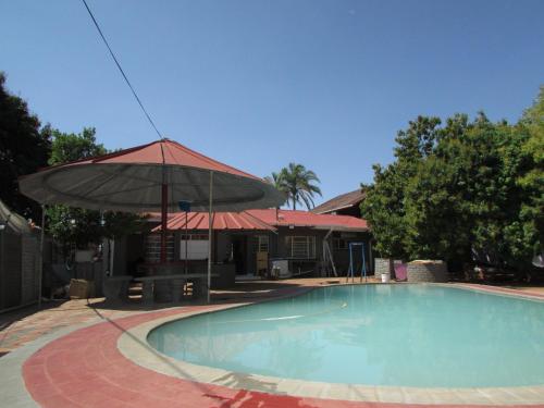 a swimming pool with an umbrella next to a house at Mokopane at Freedom City Lodge in Mokopane