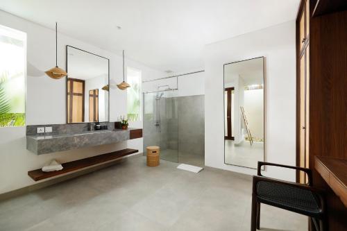 een badkamer met een douche, een wastafel en spiegels bij OMEKALI Canggu by Nakula in Canggu