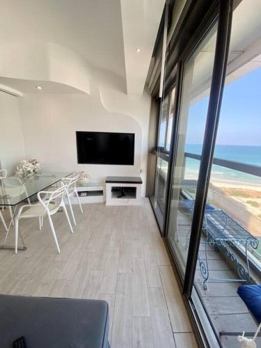 a living room with a table and a television and the ocean at ruth’s balcony sea view apt in Herzliya B