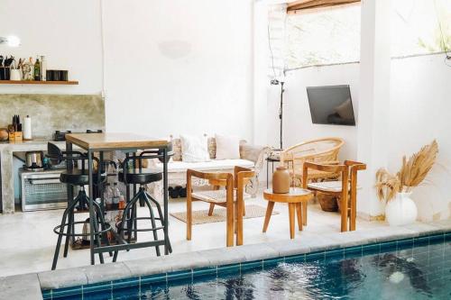 een woonkamer met een tafel en stoelen naast een zwembad bij Panayota House in Kuta Lombok