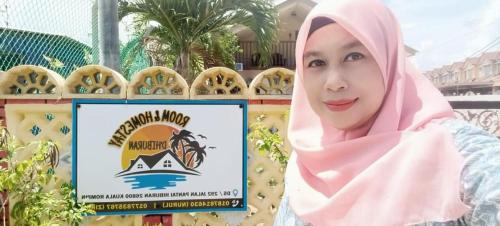 a woman in a hijab standing in front of a sign at Homestay D'Hiburan Kuala Rompin in Kuala Rompin