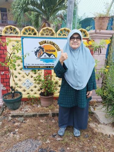an older woman standing in front of a sign at Homestay D'Hiburan Kuala Rompin in Kuala Rompin