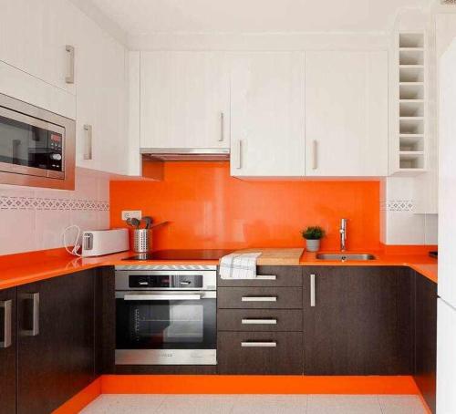 a kitchen with white cabinets and an orange wall at Coto Salinas Apartamento in Salinas