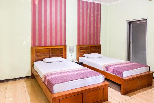 two beds in a room with red and white stripes at Global Inn Syariah Mitra RedDoorz near Juanda T1 Airport 