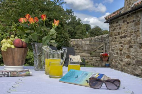 a table with glasses and a book and a vase of flowers at Swallows Nest Holiday Cottage in Cockfield