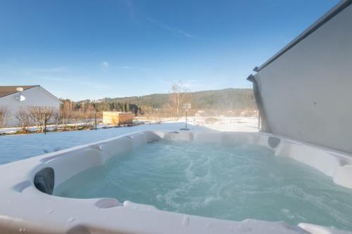 une baignoire jacuzzi dans une cour enneigée dans l'établissement Chalet du Bien-être 15p. Piscine,Spa, Hammam,Pétanque,Basket, à Gérardmer