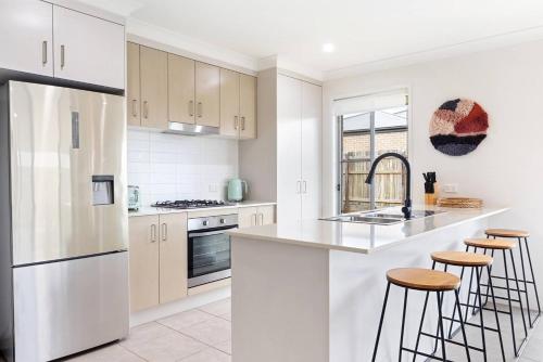 a kitchen with white cabinets and a sink and stools at 'The Pool House' Spacious Family Stay at Hervey Bay in Hervey Bay