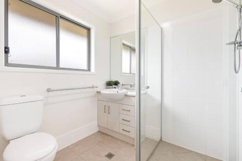 a white bathroom with a toilet and a sink at 'The Pool House' Spacious Family Stay at Hervey Bay in Urraween