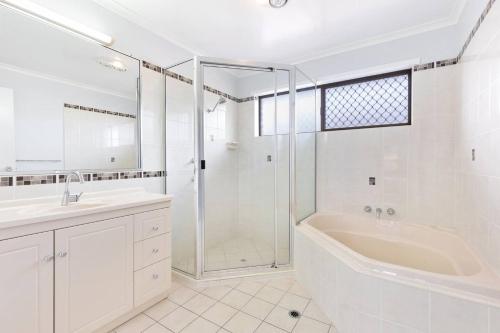 uma casa de banho branca com um chuveiro, uma banheira e um lavatório. em 'The Aussie Classic' Poolside Living by the Marina em Urangan