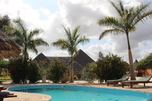 a swimming pool with palm trees in front of a house at Mapeni Lodge in Kidenge