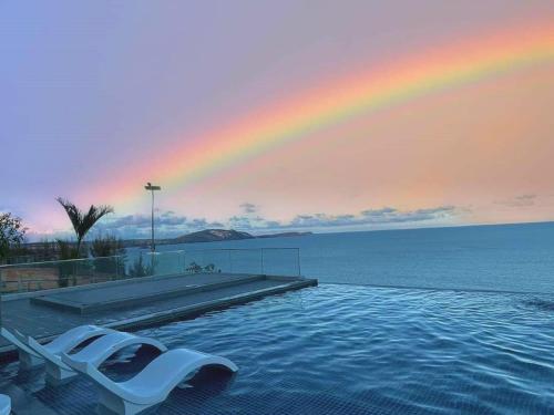a pool with a rainbow in the sky and a chair at Apec Mandala Cham Bay Condotel Mui Ne in Mui Ne