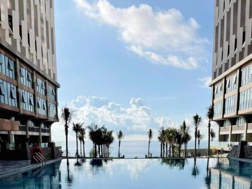 a large swimming pool between two buildings with palm trees at Apec Mandala Cham Bay Mũi Né in Mui Ne