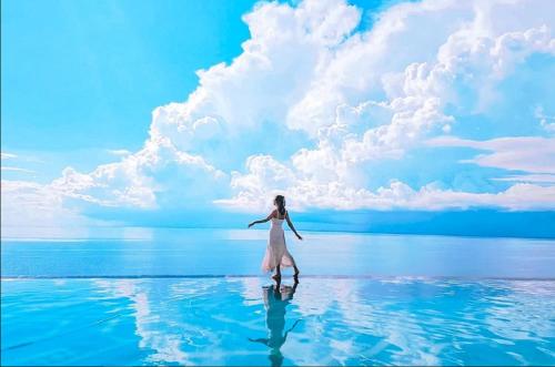a woman in a white dress walking in the water at Apec Mandala Cham Bay Condotel Mui Ne in Mui Ne