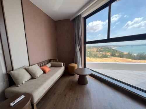 a room with a couch and a large window at Apec Mandala Cham Bay Condotel Mui Ne in Mui Ne