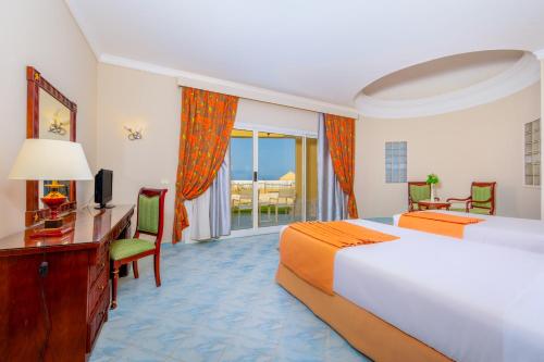 Habitación de hotel con 2 camas, escritorio y TV. en Siva Golden Bay Makadi en Hurghada
