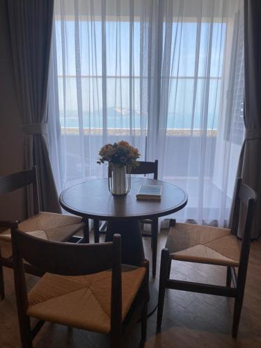 a table with a vase of flowers on it in front of a window at Apec Mandala Cham Bay Condotel Mui Ne in Mui Ne