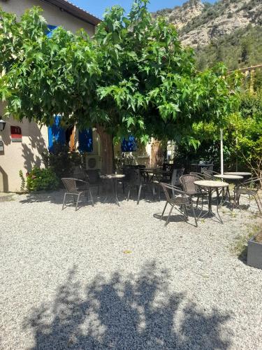 a group of tables and chairs under a tree at Hôtel Les Alizés in Puget-Théniers