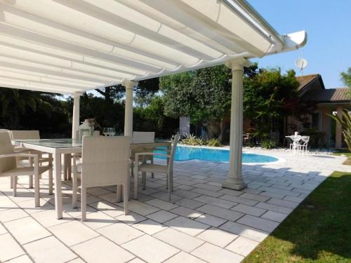 a white pergola with a table and chairs next to a pool at Wonderful villa with swimming pool on Albarella in Palazzo Vianello