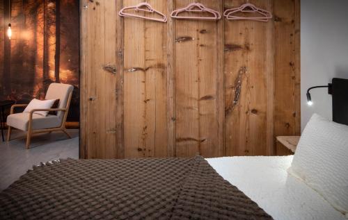 een slaapkamer met een houten muur met een bed en een stoel bij Hôtel-Restaurant Le Cochon Rose in La Sagne