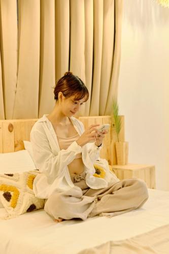 a woman sitting on a bed looking at her cell phone at Pallet Homes - Landheights Tropics in Iloilo City