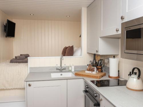 a kitchen with white cabinets and a bed in the background at Hillside Hut in Ashbourne